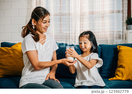 In their comfortable home an Asian mother shares a glass of milk with her daughter on the sofa. This heartening moment emphasizes the importance of calcium care and happiness. 123982779