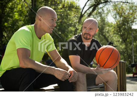 Two basketball players sitting on bench and discussing game on sports court. Sports competition game. Outdoor workout. Team sport. Basketball coach. Two basketball players sitting on bench and discussing game on sports court. Sports competition game. Outdoor workout. Team sport. Basketball coach. 123983242