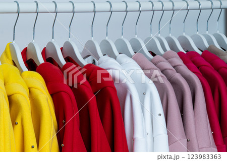 A vibrant collection of jackets hangs neatly on hangers, showcasing a spectrum of colors including yellow, red, pink, and white, set against a simple backdrop. 123983363