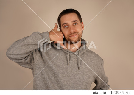 His cheerful look adds personality to the scene. The image highlights a casual and lighthearted vibe. A playful man mimics a phone call by holding his hand near his ear. His cheerful look adds personality to the scene. The image highlights a casual and lighthearted vibe. A playful man mimics a phone call by holding his hand near his ear. 123985163