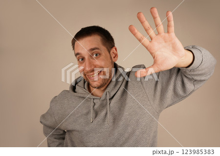 A man raises his open palm in a friendly greeting or farewell. His warm expression enhances the welcoming gesture. The scene conveys positivity and approachability. A man raises his open palm in a friendly greeting or farewell. His warm expression enhances the welcoming gesture. The scene conveys positivity and approachability. 123985383
