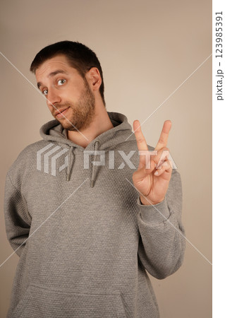 His relaxed pose symbolizes calm and goodwill. The gesture speaks of peace and togetherness. The boy in a grey hoodie flashes a peace sign, holding up his fingers in a "V" shape. His relaxed pose symbolizes calm and goodwill. The gesture speaks of peace and togetherness. The boy in a grey hoodie flashes a peace sign, holding up his fingers in a "V" shape. 123985391