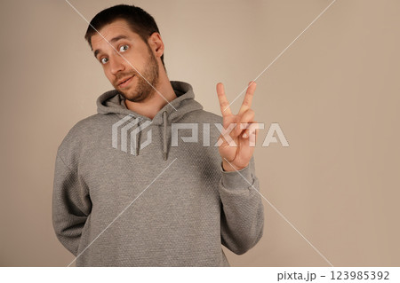 The gesture speaks of peace and togetherness. The boy in a grey hoodie flashes a peace sign, holding up his fingers in a "V" shape. His relaxed pose symbolizes calm and goodwill. 123985392