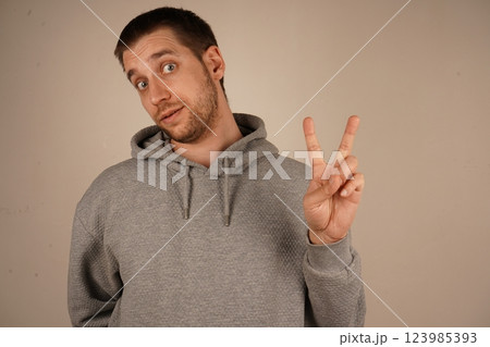 His relaxed pose symbolizes calm and goodwill. The gesture speaks of peace and togetherness. The boy in a grey hoodie flashes a peace sign, holding up his fingers in a "V" shape. 123985393