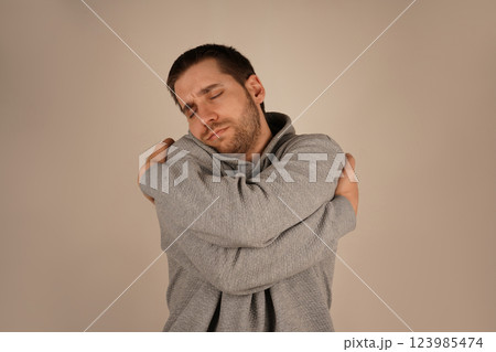 His embrace highlights emotional comfort and self-affection. It s a tender, cozy moment. With a light beard, the young man holds himself close, offering a sense of warmth and serenity. 123985474