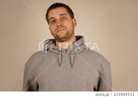 A bearded man in a gray hoodie is shown up close. His face is framed by his full beard, giving him a rugged yet casual look. The hoodie adds to his relaxed, stylish appearance. 123985511