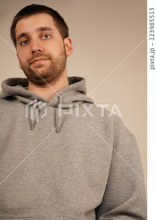 His face shows a relaxed demeanor, giving off a casual vibe. The side view of a man in a grey hoodie highlights his short dark hair and light stubble. 123985513