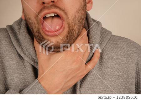 A man grips his throat with his hand, mouth wide open as if he s choking or coughing. The discomfort on his face shows the urgency of the moment, as he struggles with breathing or a strong cough. A man grips his throat with his hand, mouth wide open as if he s choking or coughing. The discomfort on his face shows the urgency of the moment, as he struggles with breathing or a strong cough. 123985610