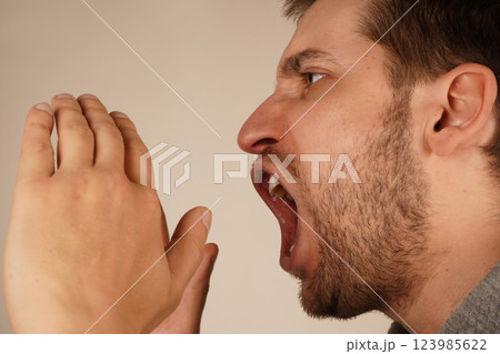 His actions suggest a loud announcement. The image conveys excitement and energy. With dark hair and a lively expression, the man cups both hands over his mouth, resembling a megaphone. 123985622