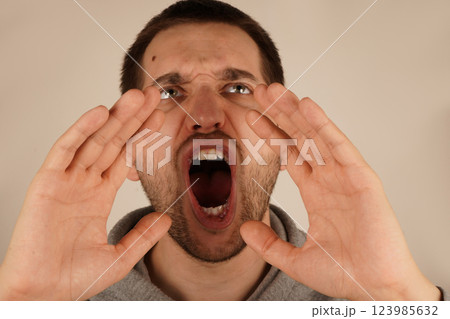 The scene captures his dramatic gesture. A young man with dark hair places his hands near his mouth, resembling a megaphone. His enthusiastic pose suggests he is delivering an energetic shout. 123985632