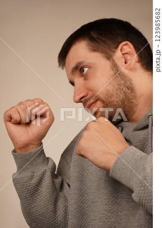 His posture suggests readiness and determination. The image conveys a strong and focused attitude. A man in a sporty hoodie stands with clenched fists in a boxing stance. 123985682