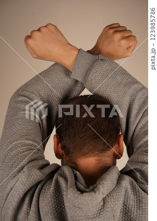 A rear view of a man with arms crossed above his head, forming clenched fists. His posture exudes confidence and strength. The scene highlights power and determination. A rear view of a man with arms crossed above his head, forming clenched fists. His posture exudes confidence and strength. The scene highlights power and determination. 123985786
