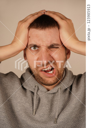 A man holds both hands on his head, a gesture that indicates stress or mental tension. His facial expression reflects the weight of his thoughts. The image captures the feeling of pressure and anxiety 123985913