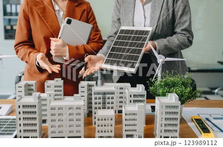 Team of diverse multiethnic businesspeople standing neare table looking at model of building from residential project. Team of diverse multiethnic businesspeople standing neare table looking at model of building from residential project. 123989112