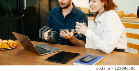 Modern couple collaborating over coffee in a cozy kitchen setting with a laptop, notebook, and breakfast. 123990306