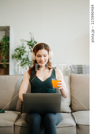 Happy woman with headphones using a laptop in a cozy living room with food and drink. Perfect for themes Happy woman with headphones using a laptop in a cozy living room with food and drink. Perfect for themes 123990484
