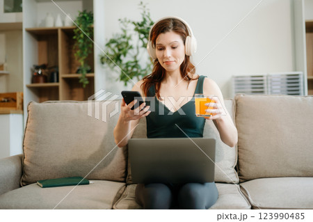 Happy woman with headphones using a laptop in a cozy living room with food and drink. Perfect for themes 123990485