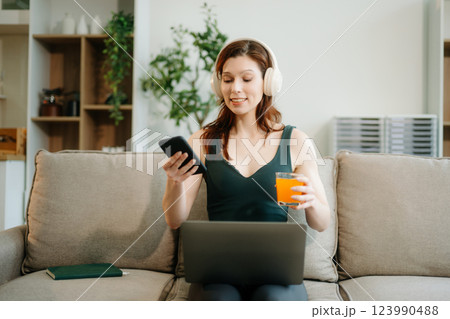 Happy woman with headphones using a laptop in a cozy living room with food and drink. Perfect for themes Happy woman with headphones using a laptop in a cozy living room with food and drink. Perfect for themes 123990488