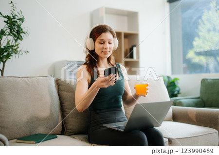 Happy woman with headphones using a laptop in a cozy living room with food and drink. Perfect for themes 123990489
