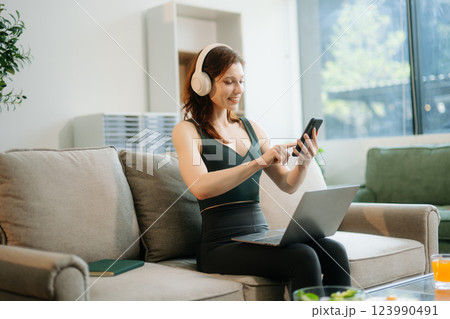 Happy woman with headphones using a laptop in a cozy living room with food and drink. Perfect for themes Happy woman with headphones using a laptop in a cozy living room with food and drink. Perfect for themes 123990491