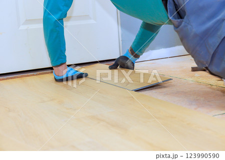 Carpenter carefully lays down laminate flooring in room during home renovation Carpenter carefully lays down laminate flooring in room during home renovation 123990590