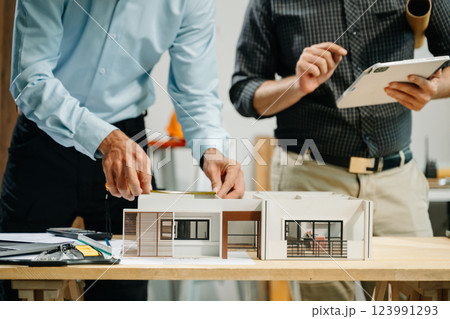 Professional collaboration in architecture. Two engineers work on construction plans, using tools like laptops, tablets, and scale models. 123991293
