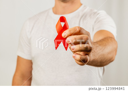 Man holding a red ribbon to raise awareness for AIDS prevention and support 123994841