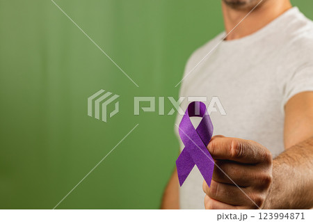 Person holding a purple ribbon against a green background to raise awareness 123994871