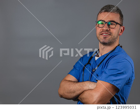 A healthcare worker stands with arms crossed, wearing blue scrubs and glasses A healthcare worker stands with arms crossed, wearing blue scrubs and glasses 123995031
