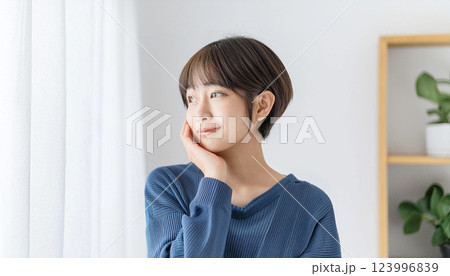 明るい窓辺で顎に手を当てている若い女性の横顔 明るい窓辺で顎に手を当てている若い女性の横顔 123996839