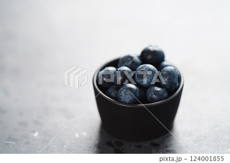 Fresh ripe blueberries in small black bowl on concrete background with copy space 124001855