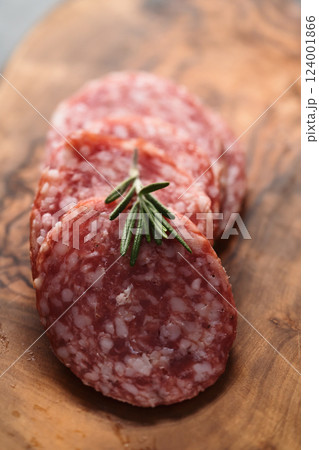 Sliced salame milano sausage on olive wood board with rosemary Sliced salame milano sausage on olive wood board with rosemary 124001866