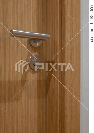 Close-up of a wooden door with a stainless steel handle and keyhole lock in modern design 124002655