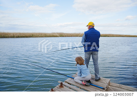 Grandfather and granddaughter on the bridge by the river with fishing rods. 124003007