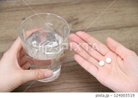 2錠の内服薬を飲もうとする女性の手とグラスの水 124003519