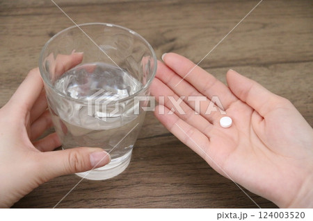 1錠の内服薬を飲もうとする女性の手とグラスの水 124003520