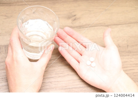 内服薬3錠を飲もうとする男性の手とグラスの水 内服薬3錠を飲もうとする男性の手とグラスの水 124004414