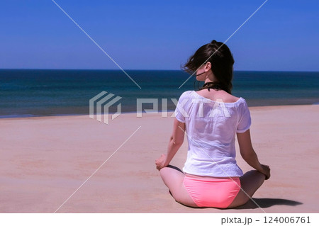 Girl meditate sits lotus pose yoga sandy beach and looks at sea back view. 124006761