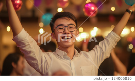 Energetic male dancer celebrating, moving dynamically with raised arms, expressing happiness amid vibrant party atmosphere 124006810