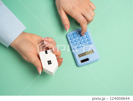 A women uses a calculator to calculate the cost of mortgage payments for a house. Household bills. Financial planning for homeownership, and evaluating household expenses. Mortgage strategies 124008644