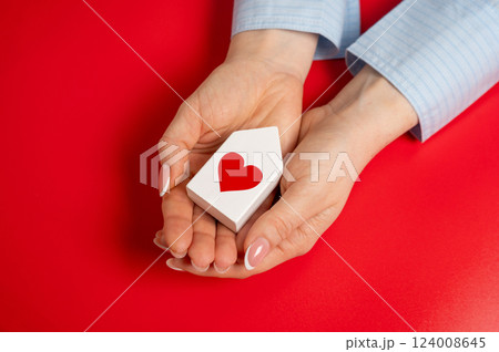 A house with a heart in the hands of a women. The concept of a love nest and the beginning of a life together. Relationship milestones, emotional security. Loving home, family bonds A house with a heart in the hands of a women. The concept of a love nest and the beginning of a life together. Relationship milestones, emotional security. Loving home, family bonds 124008645