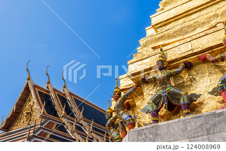Yaksha guardian statues supporting a golden stupa at Wat Phra Kaew, Bangkok, Thailand. Ornate Thai temple architecture with intricate details and vibrant decorations. 124008969