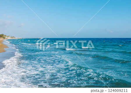 Mediterranean seascape. A picturesque sandy beach with turquoise waves gently rolling onto the shore. The azure sky, warm sand and sea foam create an atmosphere of calm and serenity 124009211