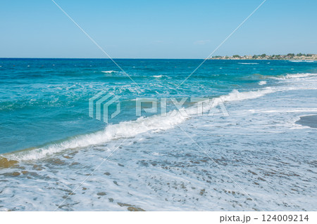 Mediterranean seascape. A picturesque sandy beach with turquoise waves gently rolling onto the shore. The azure sky, warm sand and sea foam create an atmosphere of calm and serenity Mediterranean seascape. A picturesque sandy beach with turquoise waves gently rolling onto the shore. The azure sky, warm sand and sea foam create an atmosphere of calm and serenity 124009214