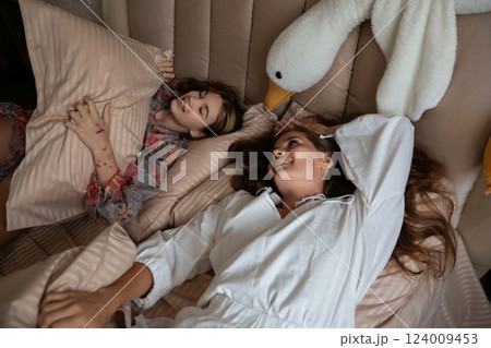 Mother Daughter Bedroom Sleep Fun: Happy mother and daughter playfully relax in bed with a plush swan toy, enjoying bedtime together. Mother Daughter Bedroom Sleep Fun: Happy mother and daughter playfully relax in bed with a plush swan toy, enjoying bedtime together. 124009453