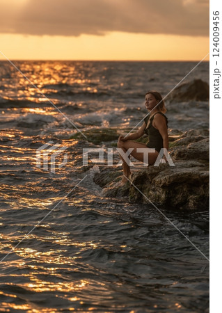 Woman Sunset Seascape - Silhouette of a woman sitting on a rock by the sea at sunset. 124009456