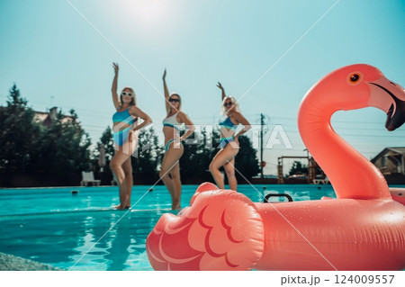Three women are in the water, one of them is holding a pink flamingo. Scene is fun and playful. 124009557