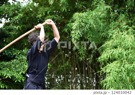 剣道着姿のシニア女性が、屋外で竹刀を持ち、一人稽古をしている 124010042
