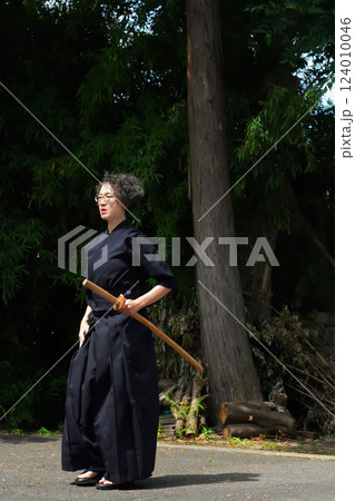 剣道着姿のシニア女性が、屋外で竹刀を持ち、一人稽古をしている 剣道着姿のシニア女性が、屋外で竹刀を持ち、一人稽古をしている 124010046
