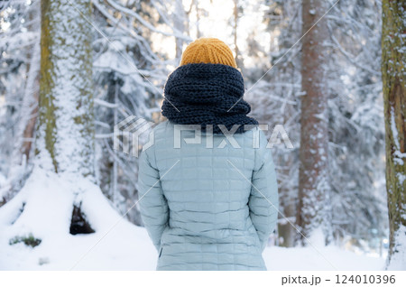 Young adult woman alone slowly walking on snow covered boardwalk after snowfall. Enjoying fresh air in park. Peaceful atmosphere in winter day. Back view Young adult woman alone slowly walking on snow covered boardwalk after snowfall. Enjoying fresh air in park. Peaceful atmosphere in winter day. Back view 124010396